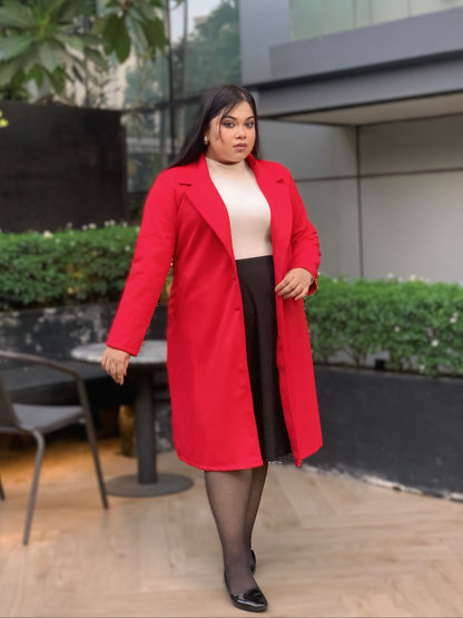 Woman wearing a red coat standing outdoors with greenery and a building in the background