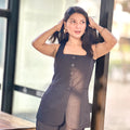 Woman wearing a sheer black outfit with buttons, standing indoors.