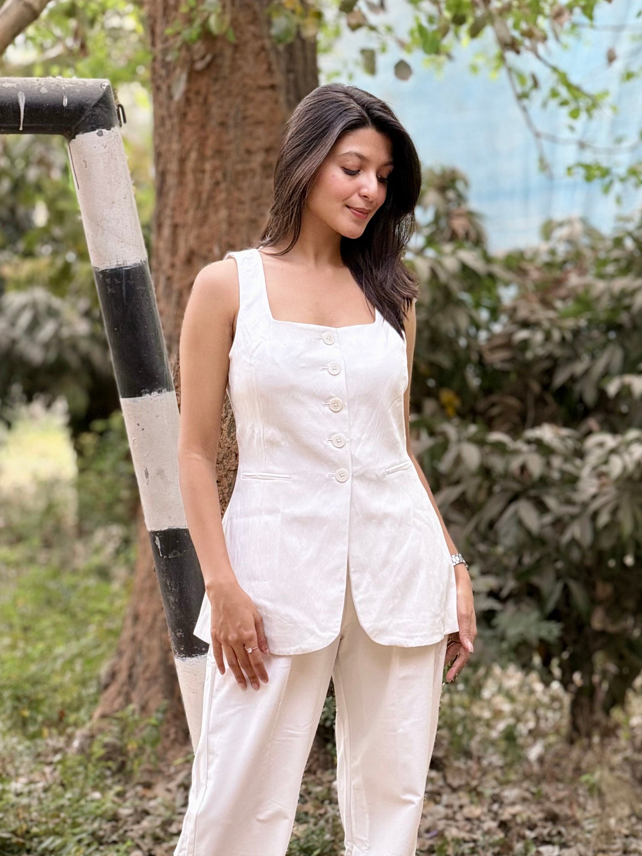 Woman in a white outfit standing outdoors near a tree