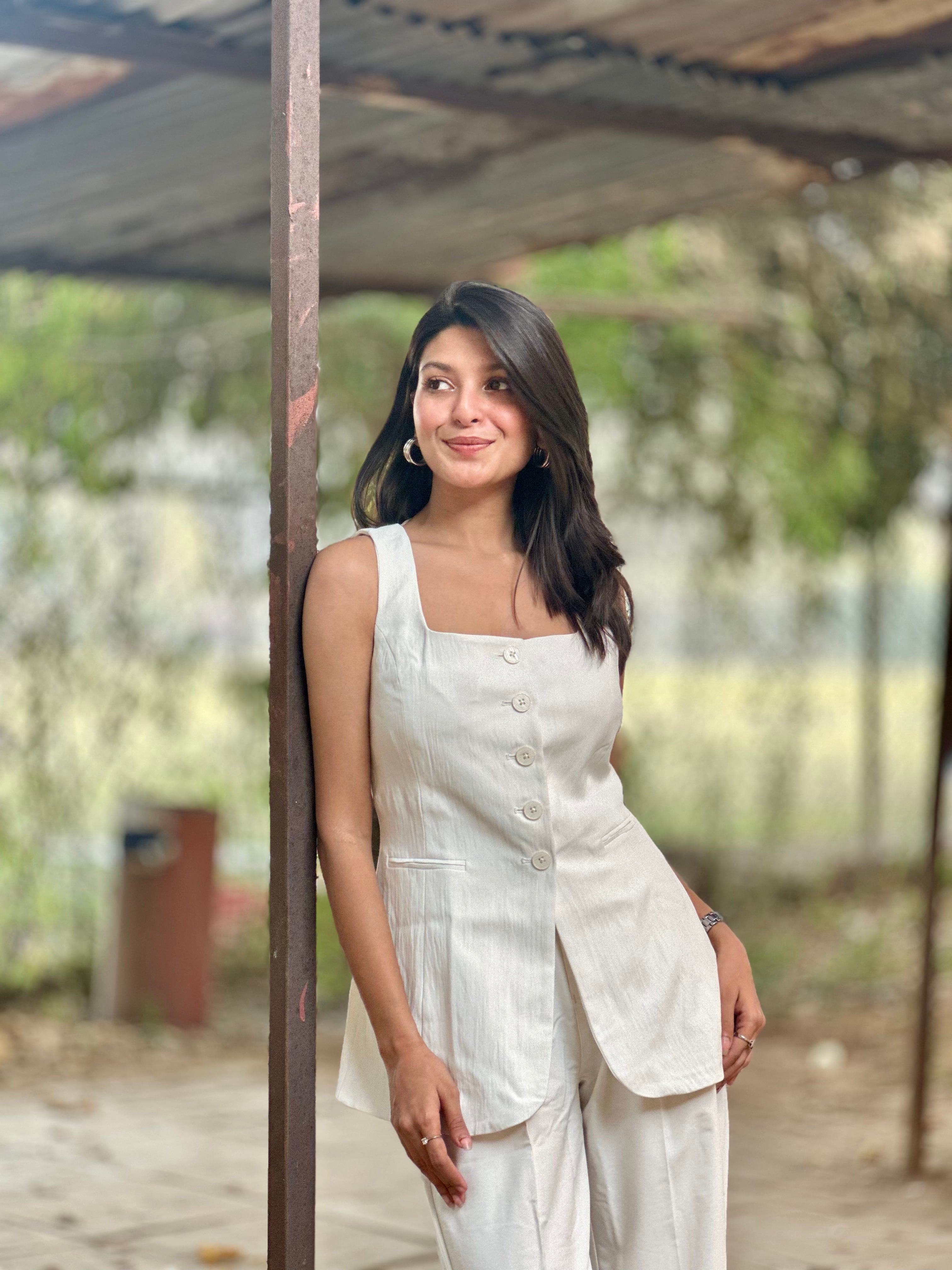 Woman in a white outfit standing under a shelter with a blurred natural background