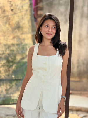 Woman wearing a white sleeveless top and light-colored pants standing outdoors.