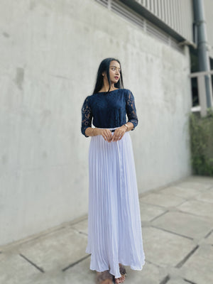 Woman wearing a navy top and white skirt standing against a concrete wall.