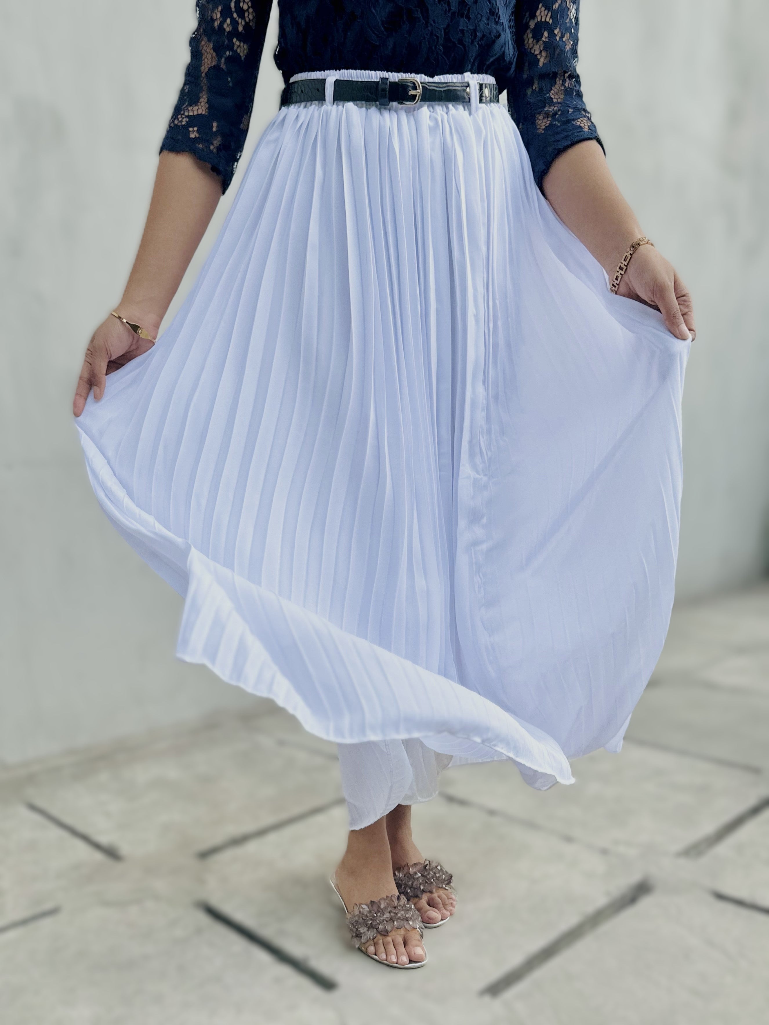 Person wearing a navy lace top and white pleated skirt on a light background
