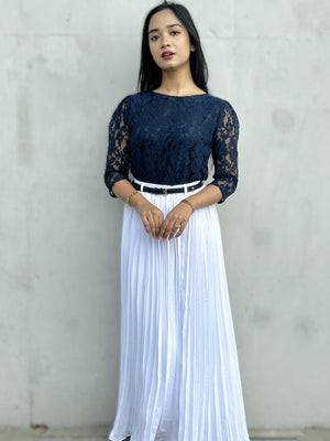 Woman wearing a navy lace top and white pleated skirt against a gray background
