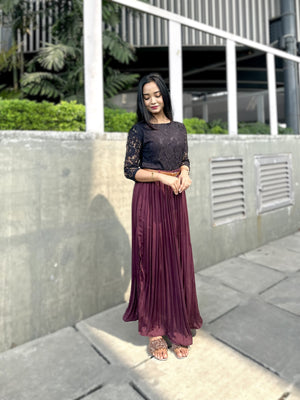 Woman in a black top and purple skirt standing outdoors near a building.