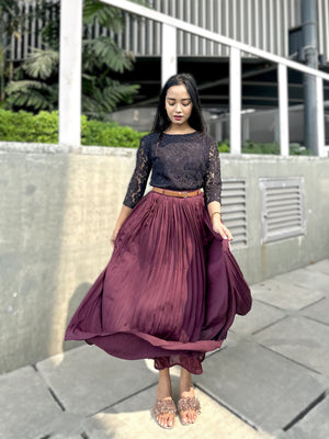 Woman wearing a dark top and long burgundy skirt standing outdoors.