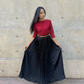 Woman wearing a red top and black pleated skirt against a concrete wall.