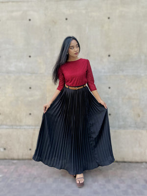 Woman wearing a red top and black pleated skirt against a concrete wall.