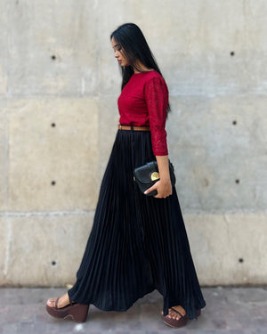 Woman wearing a red top and black pleated skirt against a concrete wall.