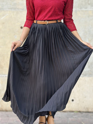 Person wearing a red top and black pleated skirt with a blurred background