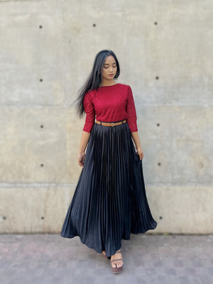 Woman wearing a red top and black pleated skirt against a textured wall.