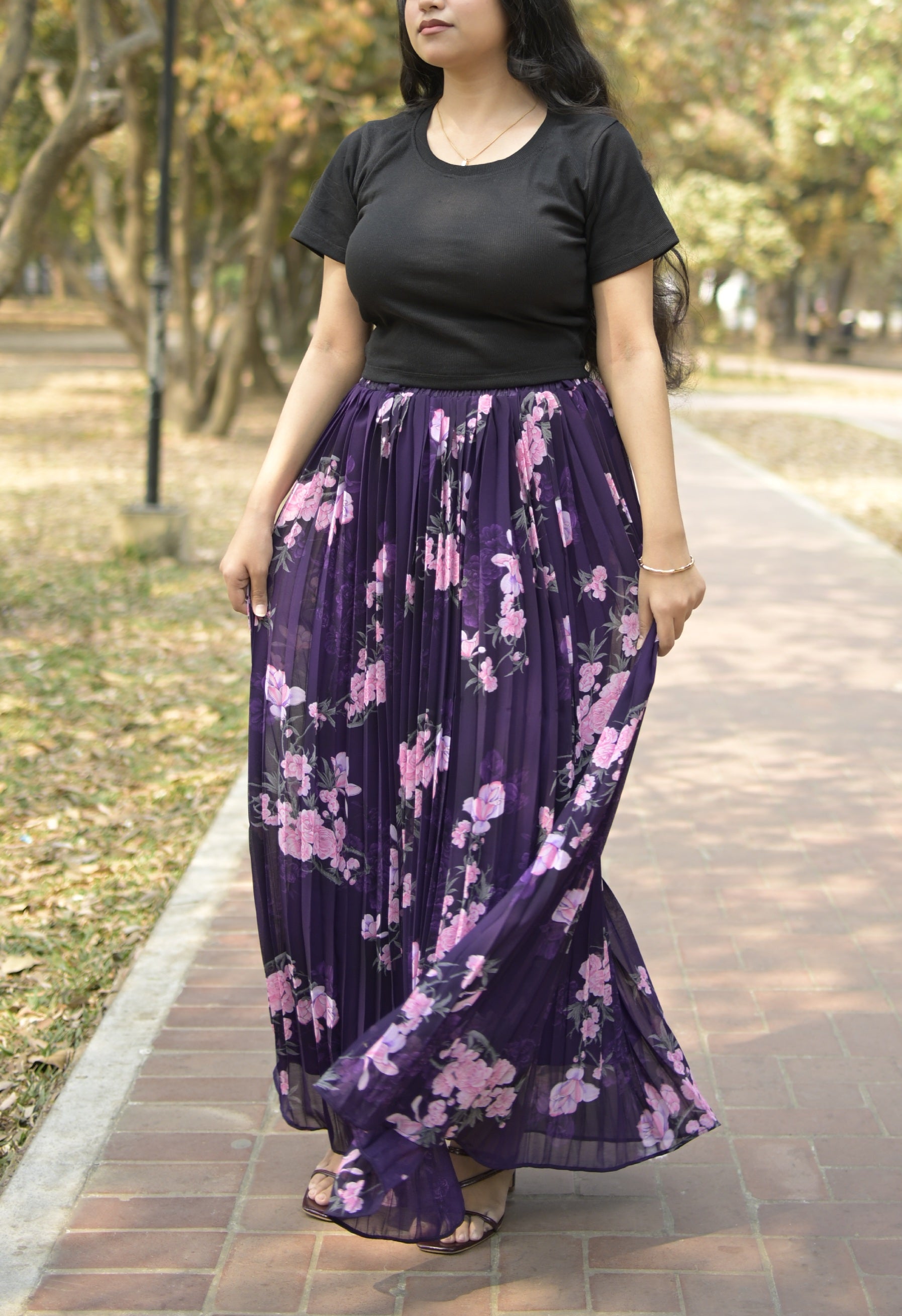Woman wearing a black top and purple floral skirt on a path with trees in the background TrendyBuzz