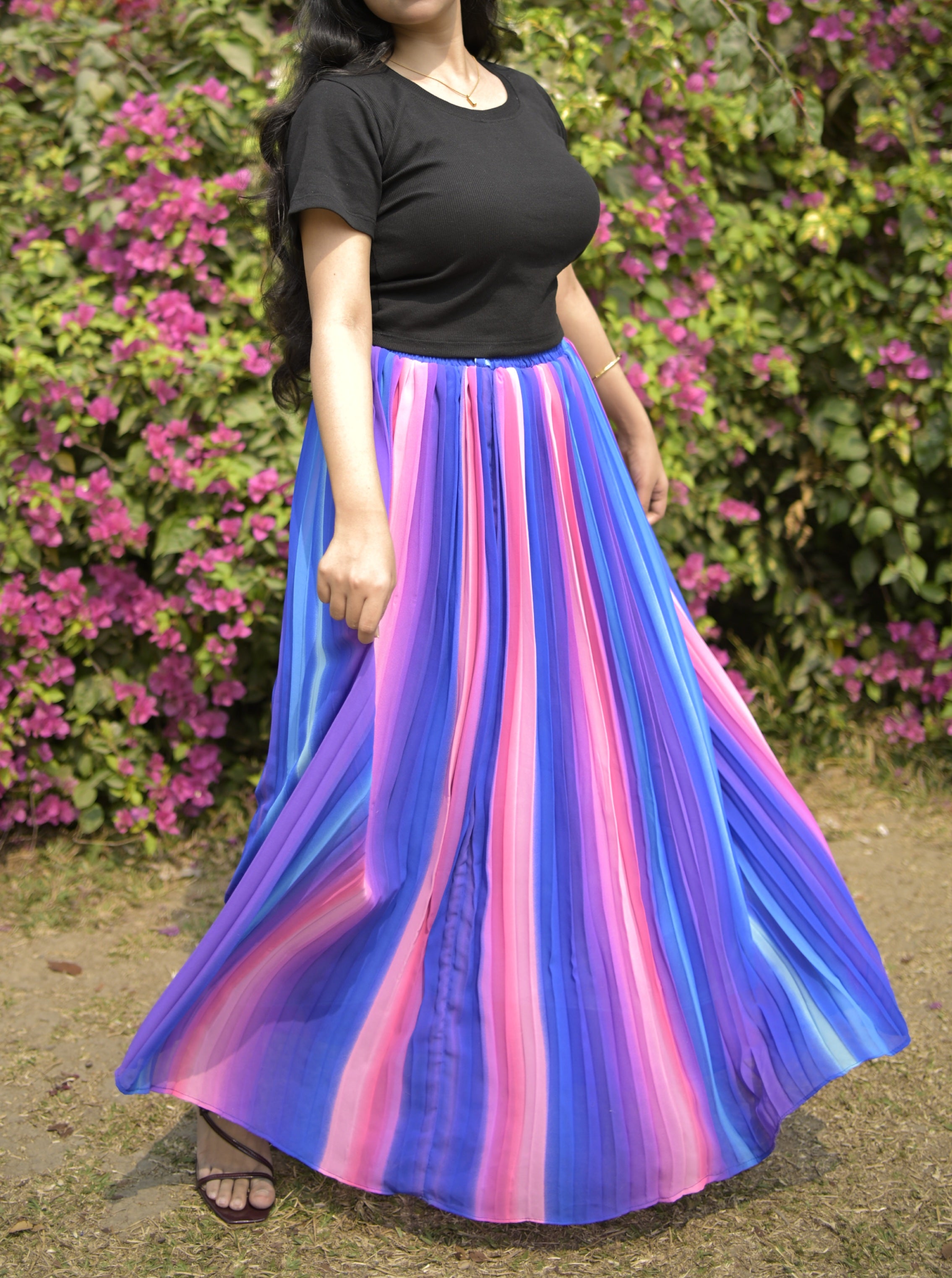 Person wearing a colorful skirt with a black top in front of pink flowers. trendy buzz