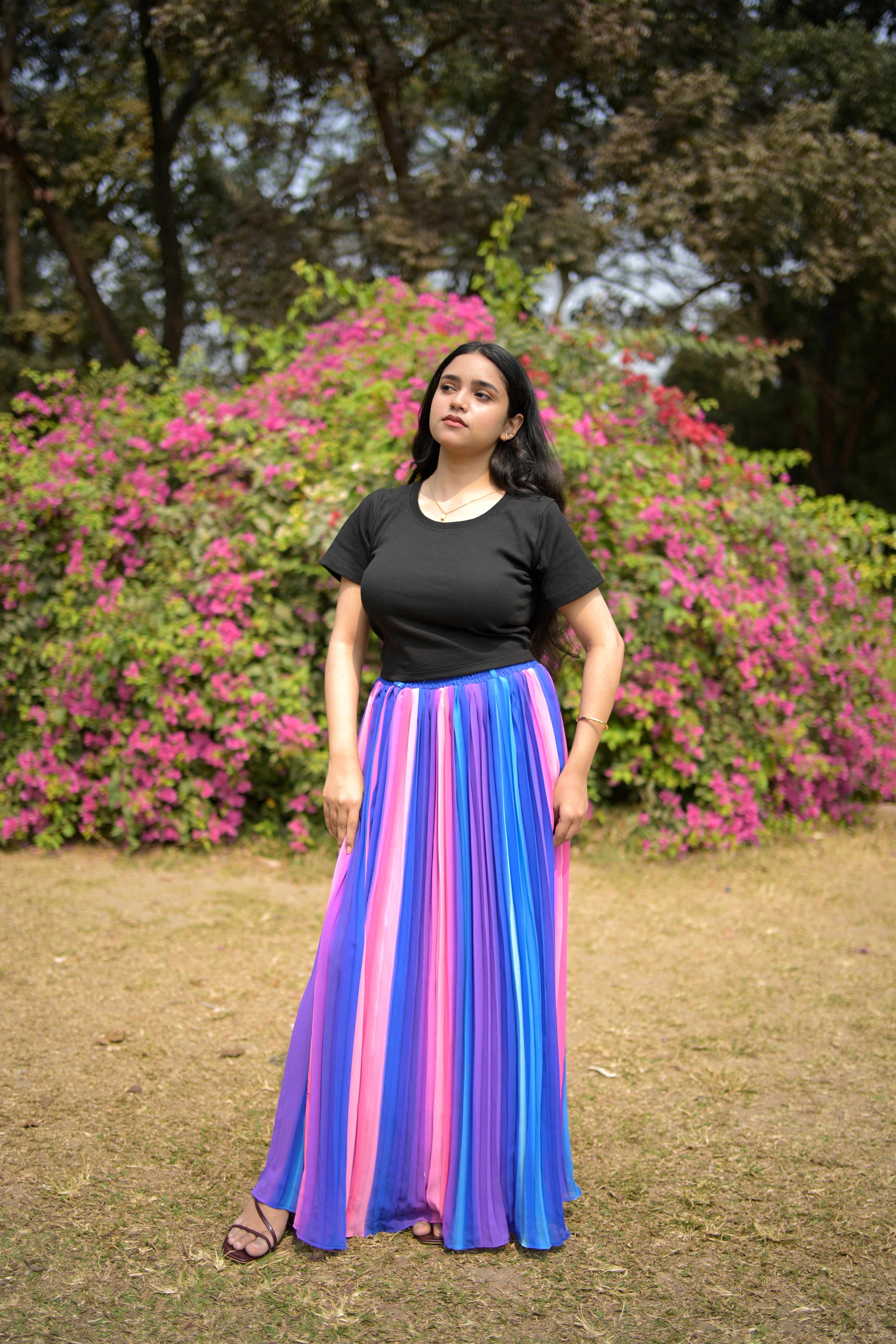 Woman in a colorful dress standing in a park with flowers and trees. trendy buzz