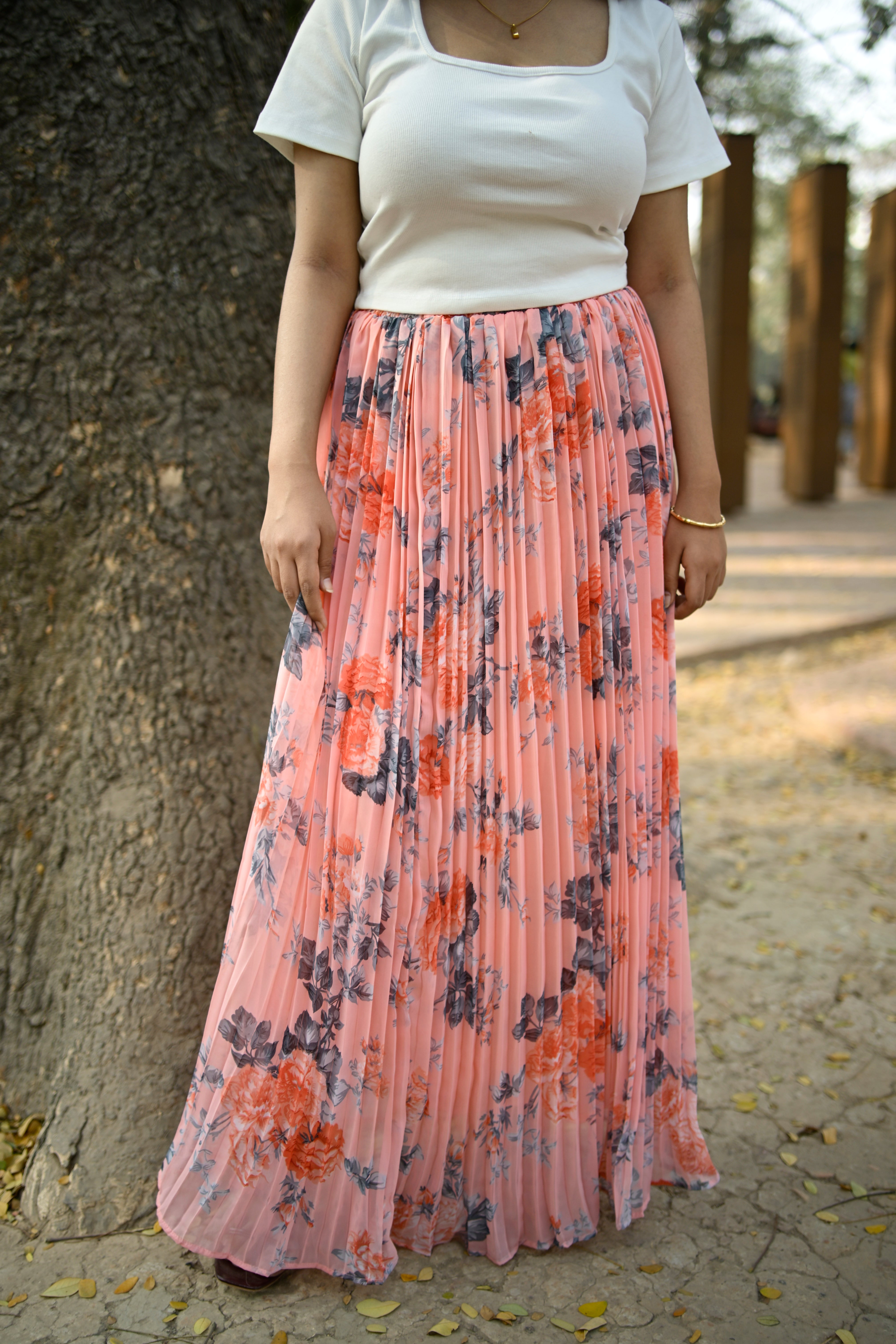 Person holding a pleated pink skirt with floral patterns against a stone wall background
