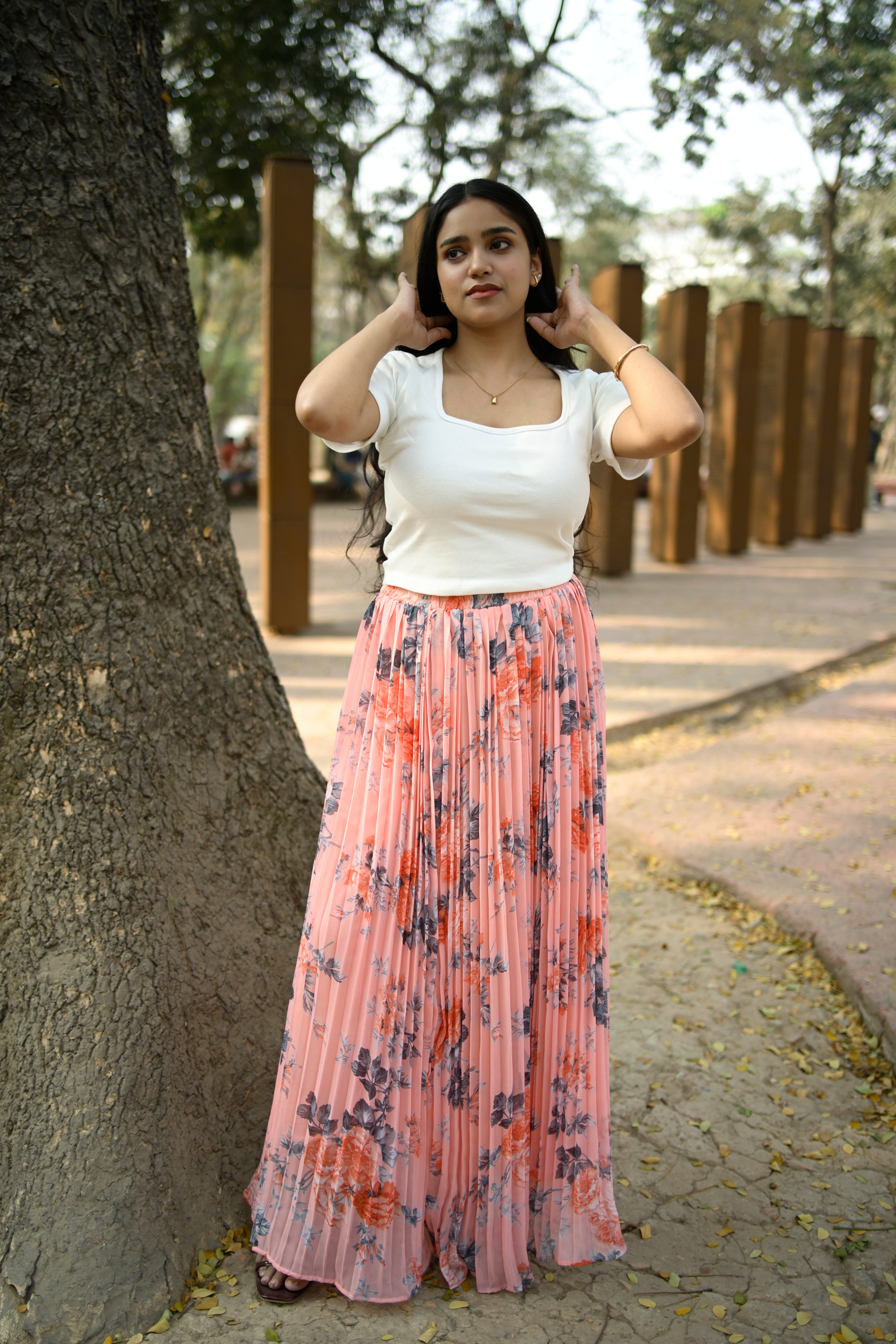 Woman in a floral skirt standing on a path next to a tree
