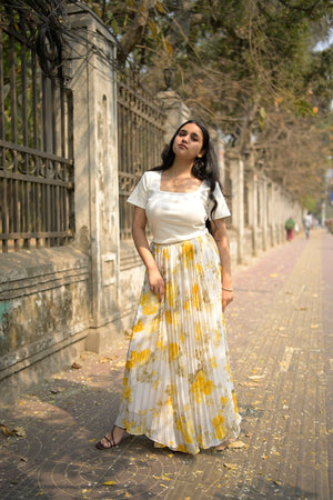 Woman in a white dress with yellow patterns standing on a stone path.