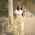Woman in a white dress with yellow floral pattern standing on a stone path.