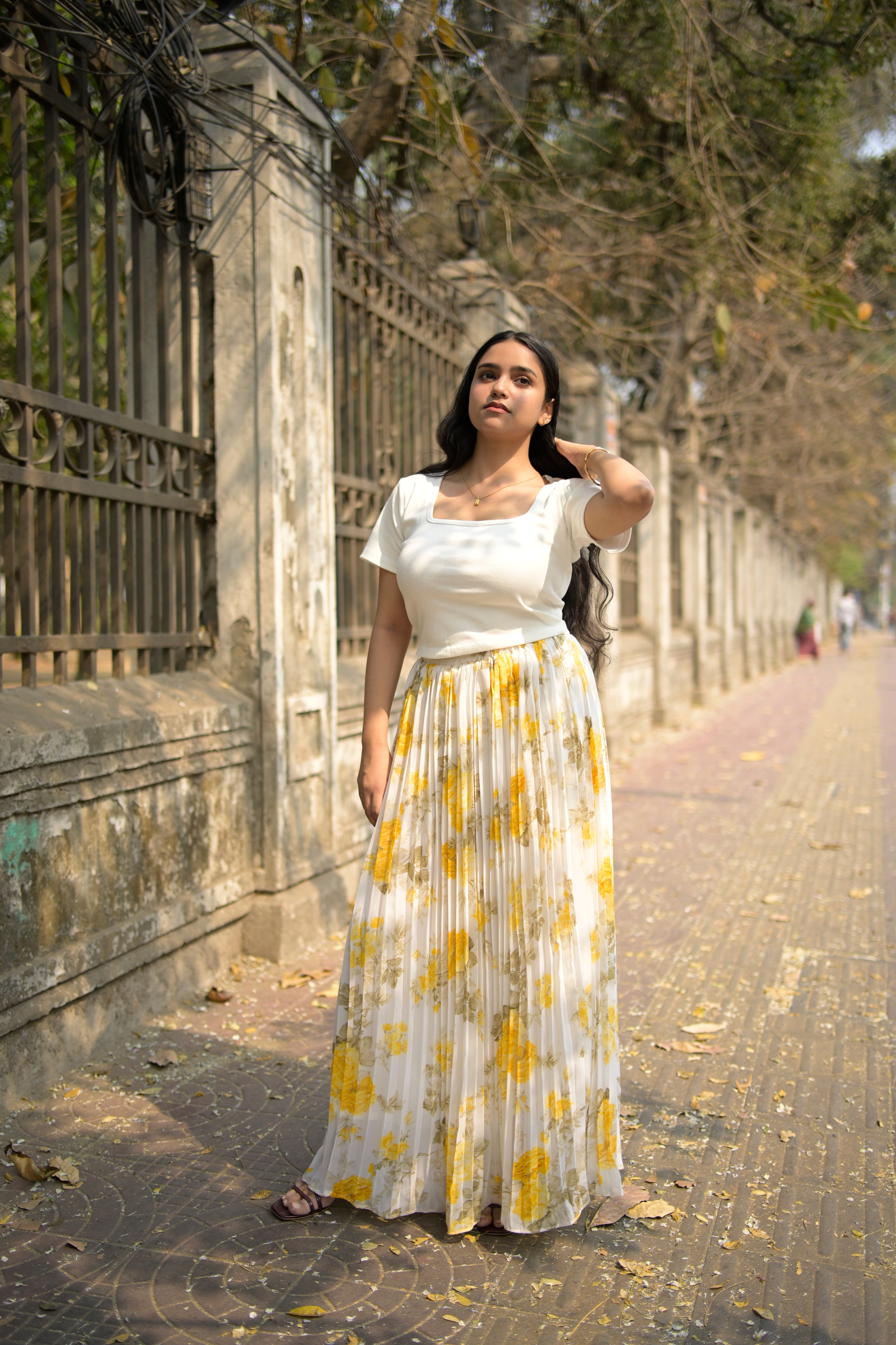 Woman in a white dress with yellow floral pattern standing on a stone path.
