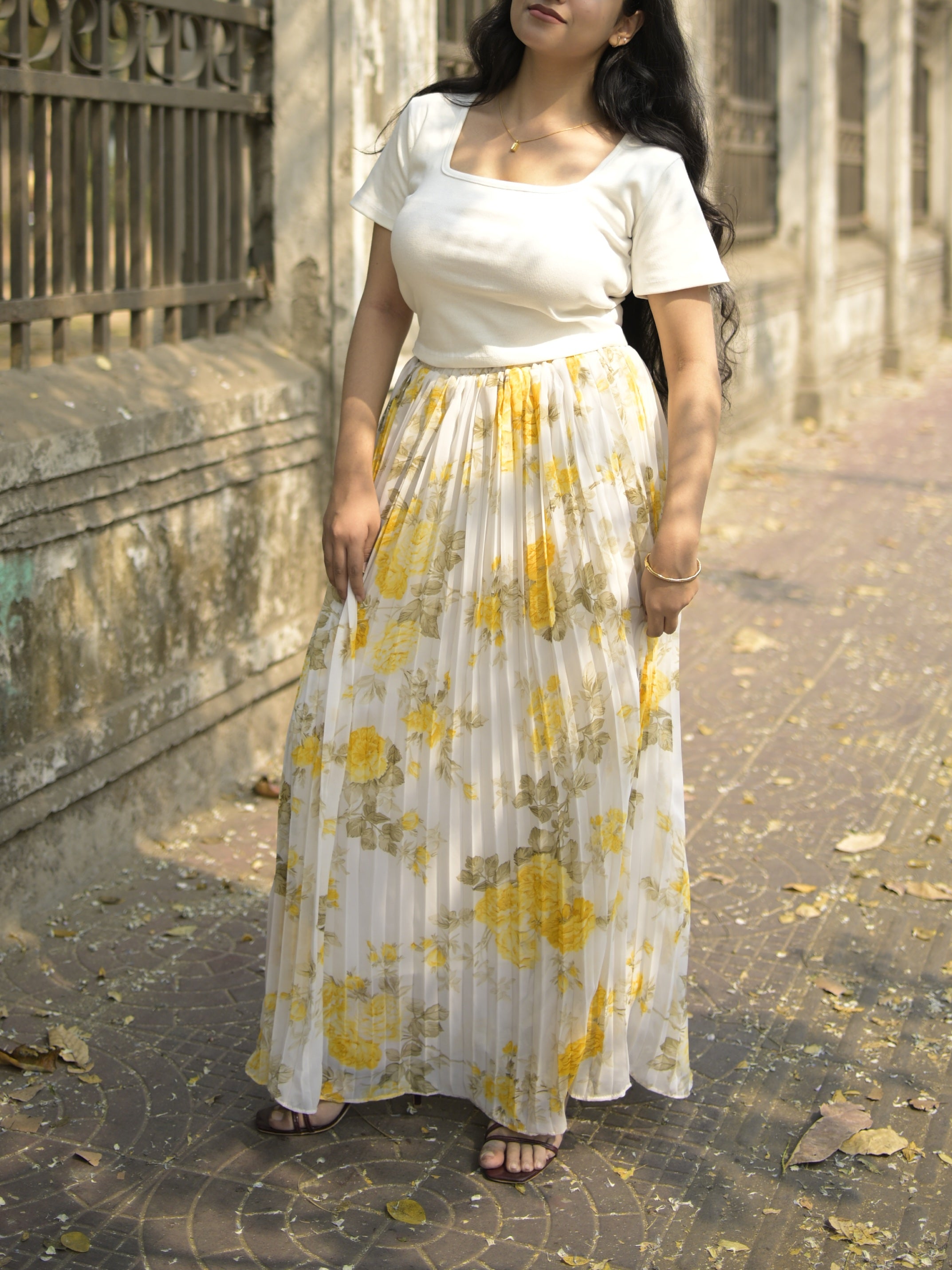 Woman wearing a white top and yellow floral skirt standing on a stone path.