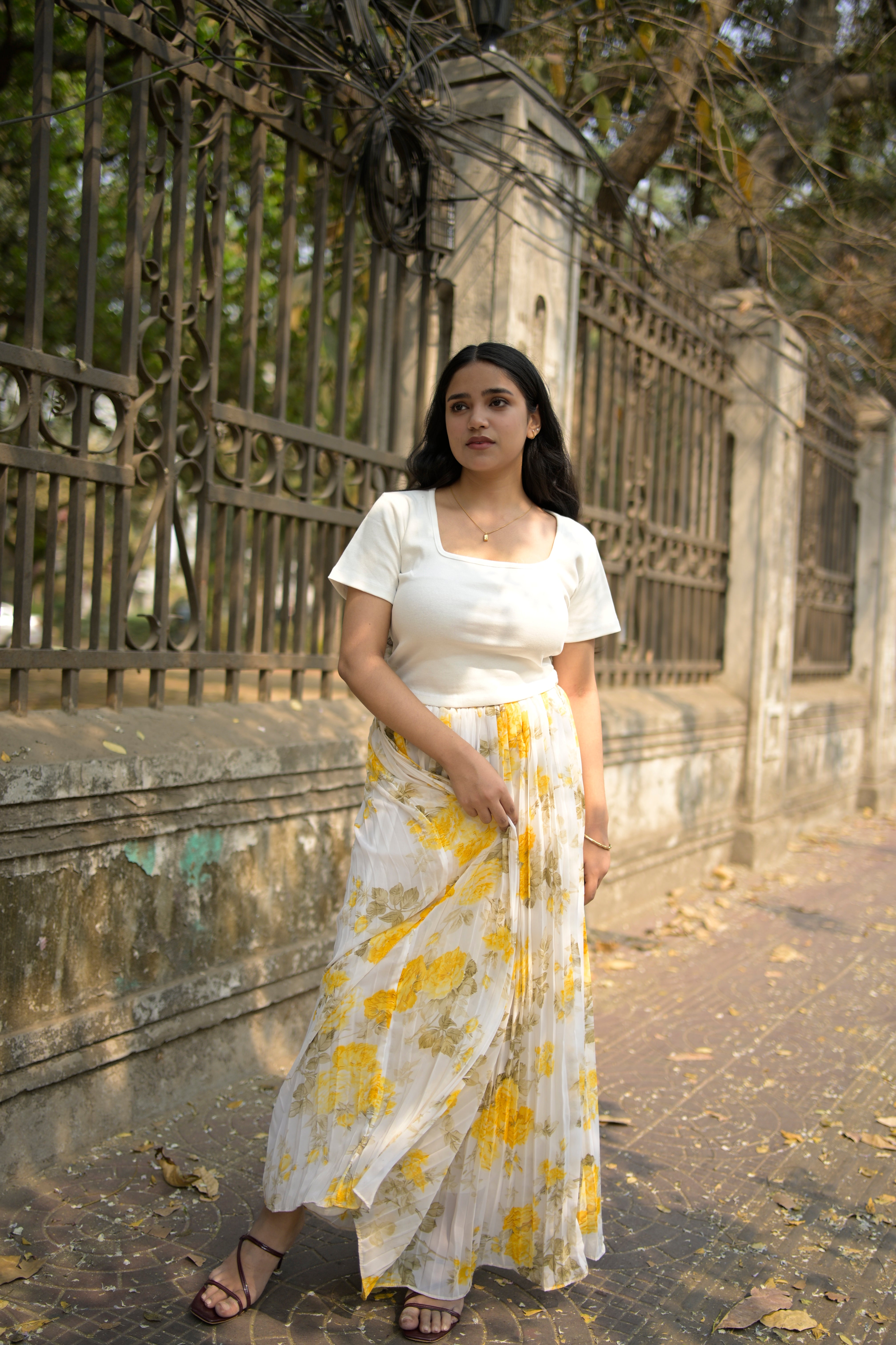 Woman in a white dress with yellow floral pattern standing on a textured surface.