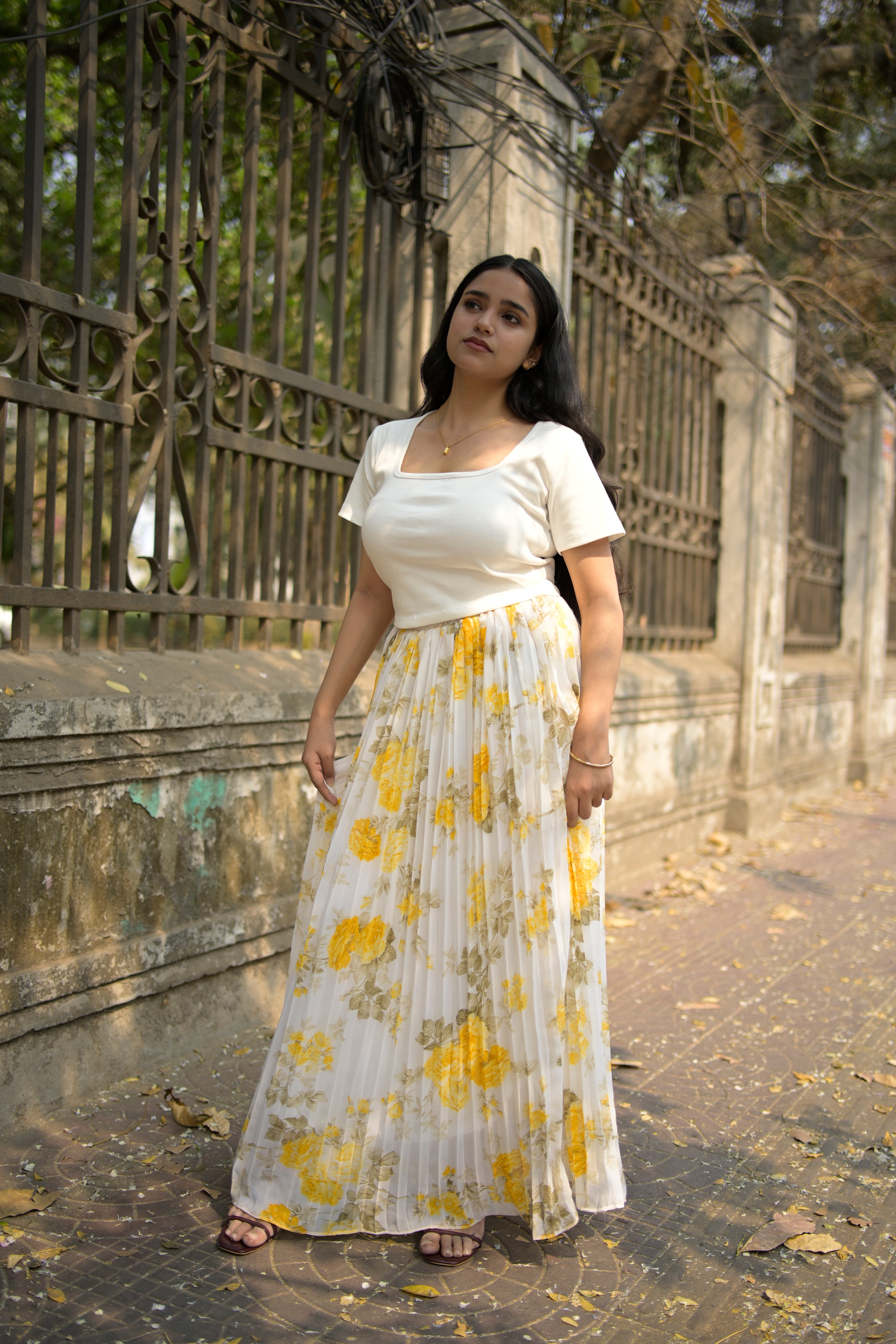 Woman in a white dress with yellow floral pattern standing in front of a textured wall.