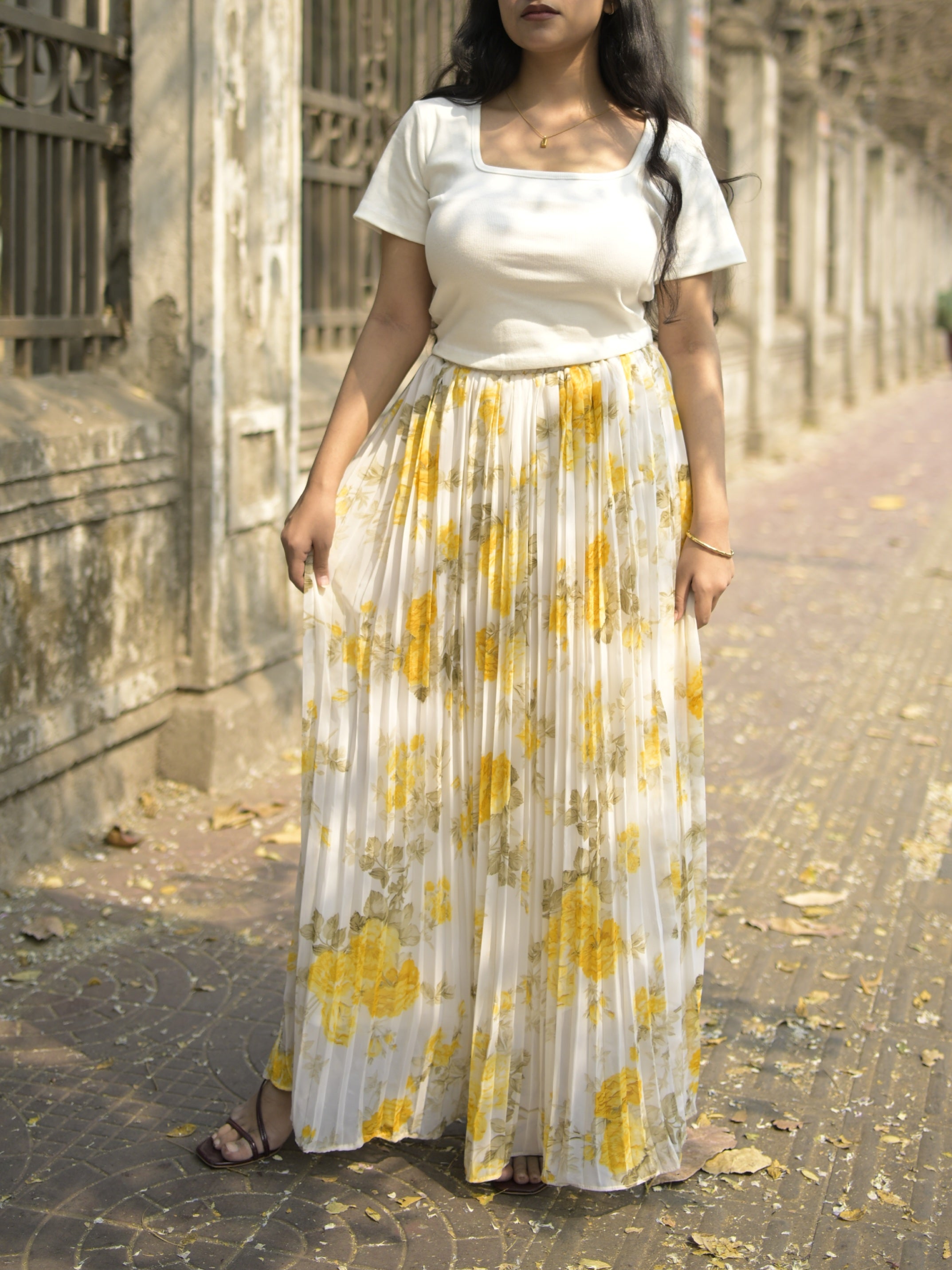 Woman wearing a white top and yellow floral skirt standing on a stone path.