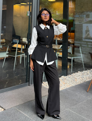 A woman models a black vest and wide-leg trousers set with a white collared shirt, standing in front of a glass storefront.