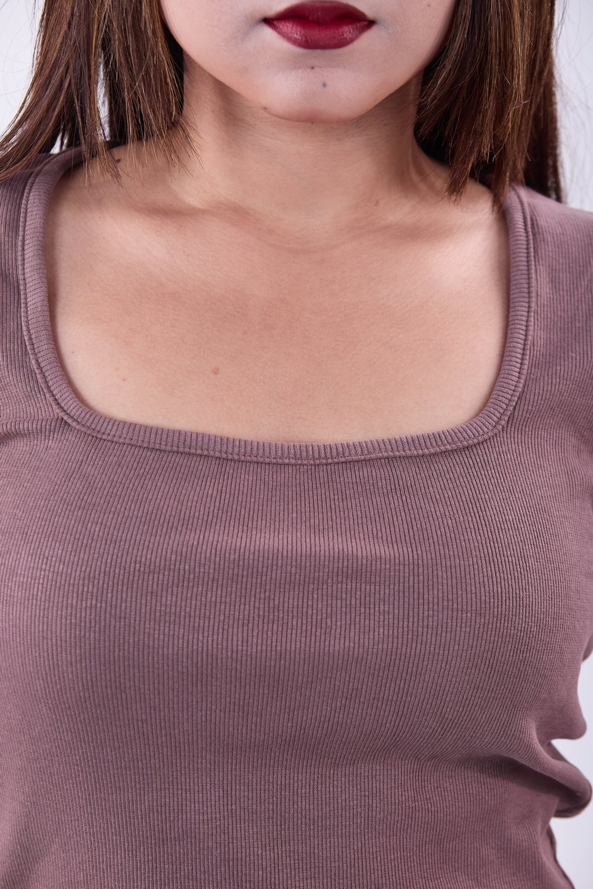 Close-up of a person wearing a mauve top with a plain background