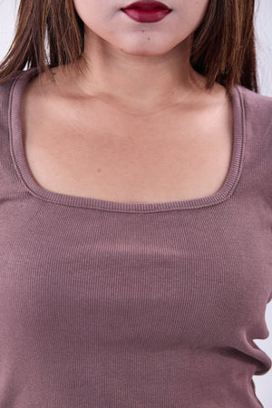 Close-up of a person wearing a mauve top with a plain background