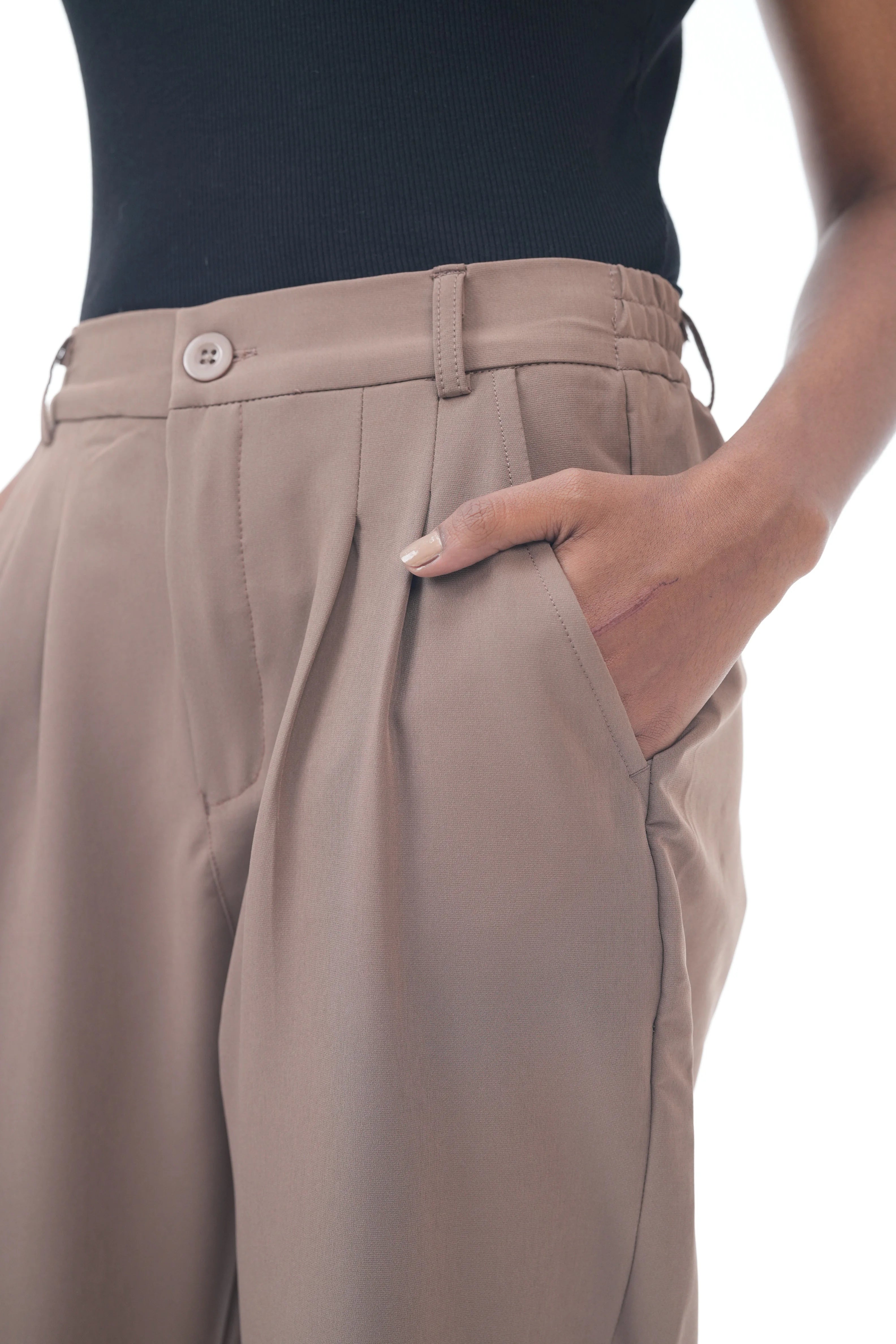 Beige pleated pants worn with a black top on a white background