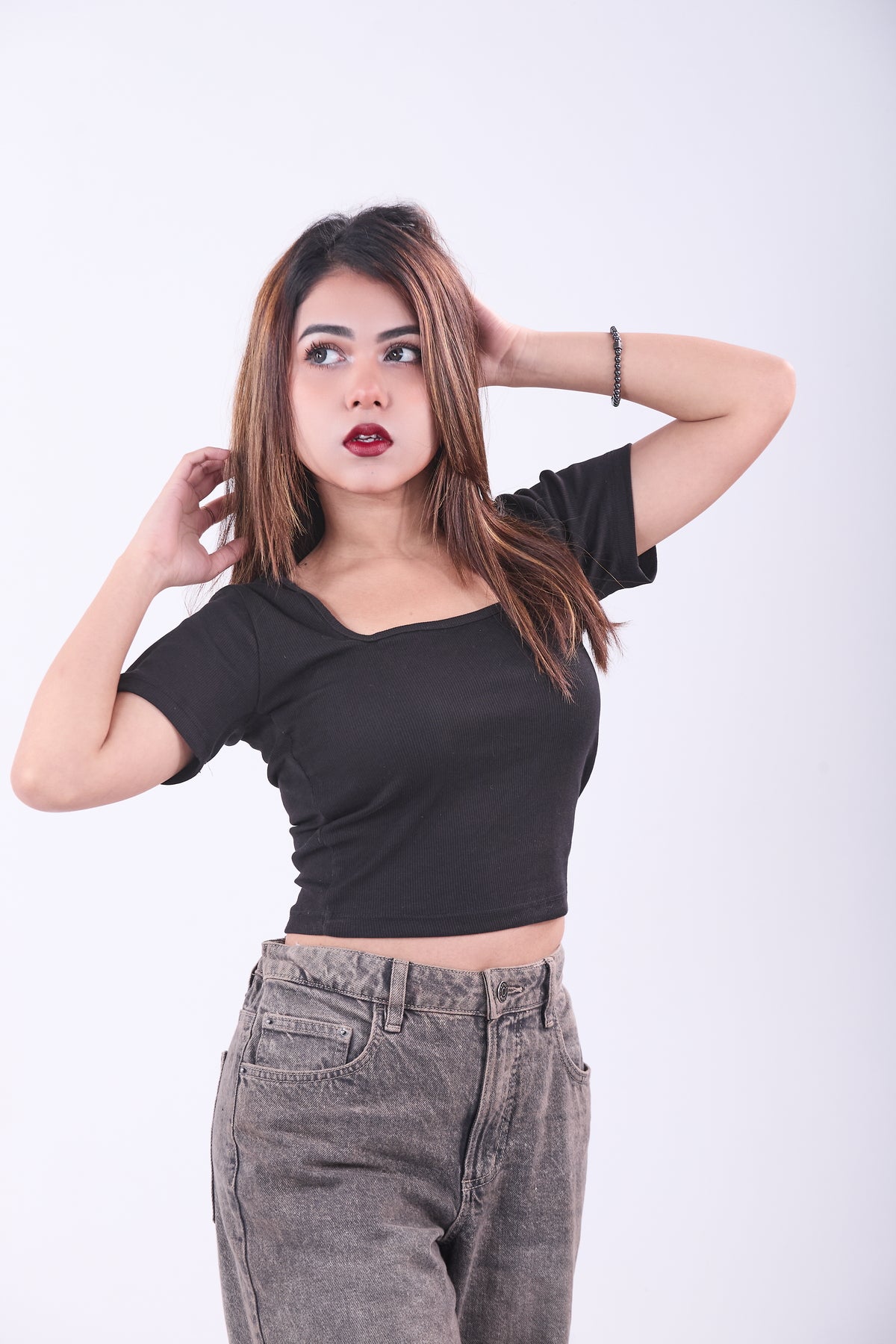 Woman wearing a black crop top and gray pants against a white background