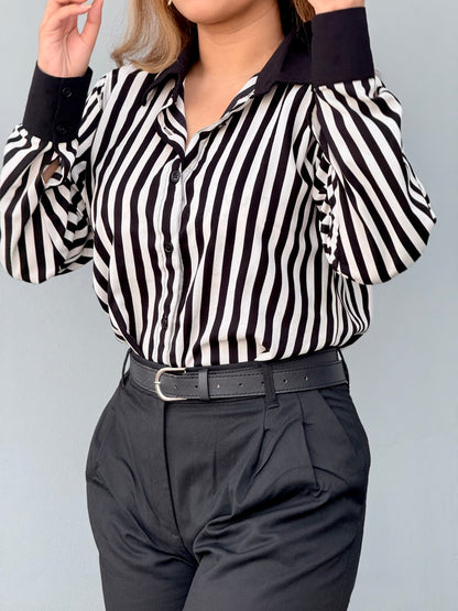 Person wearing a black and white striped shirt with long sleeves and dark pants on a light gray background