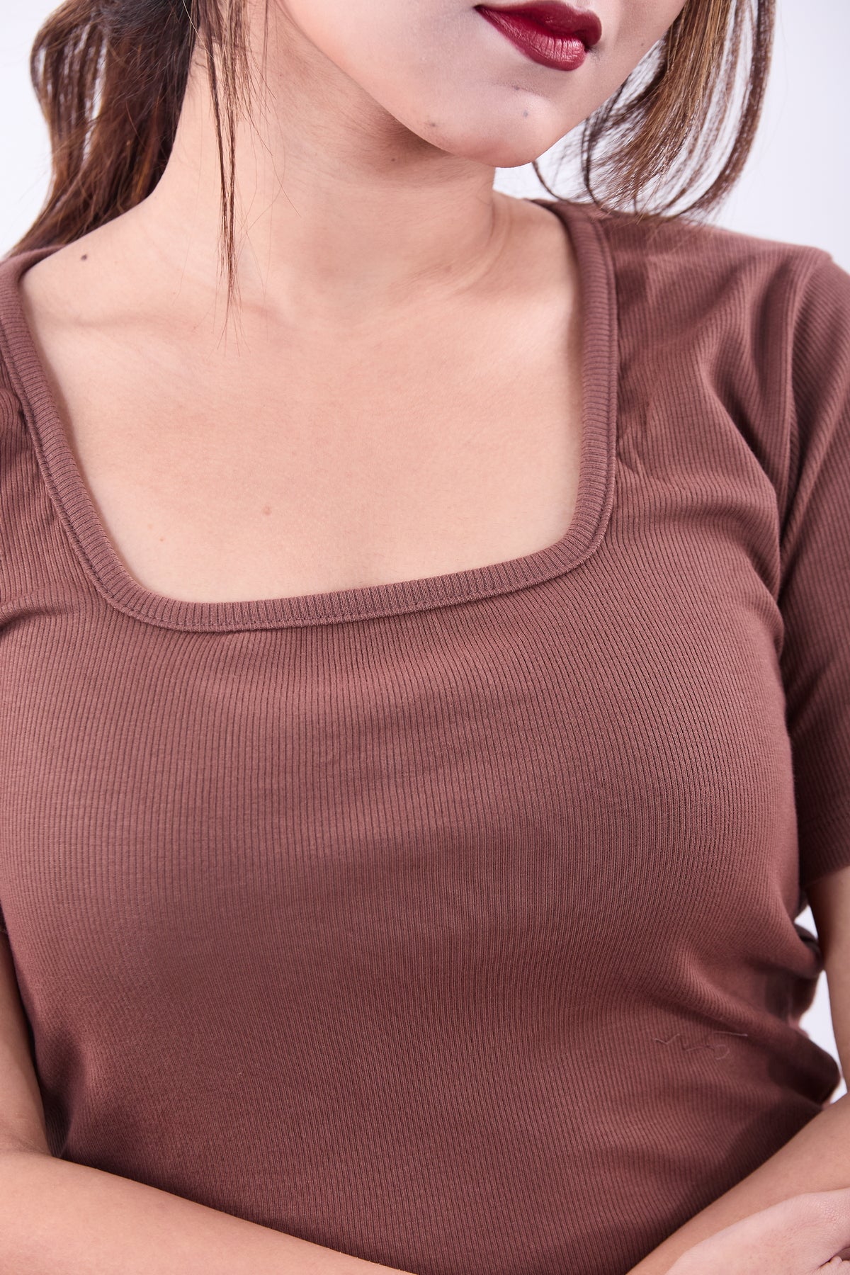 Close-up of a person wearing a brown ribbed top with a square neckline.