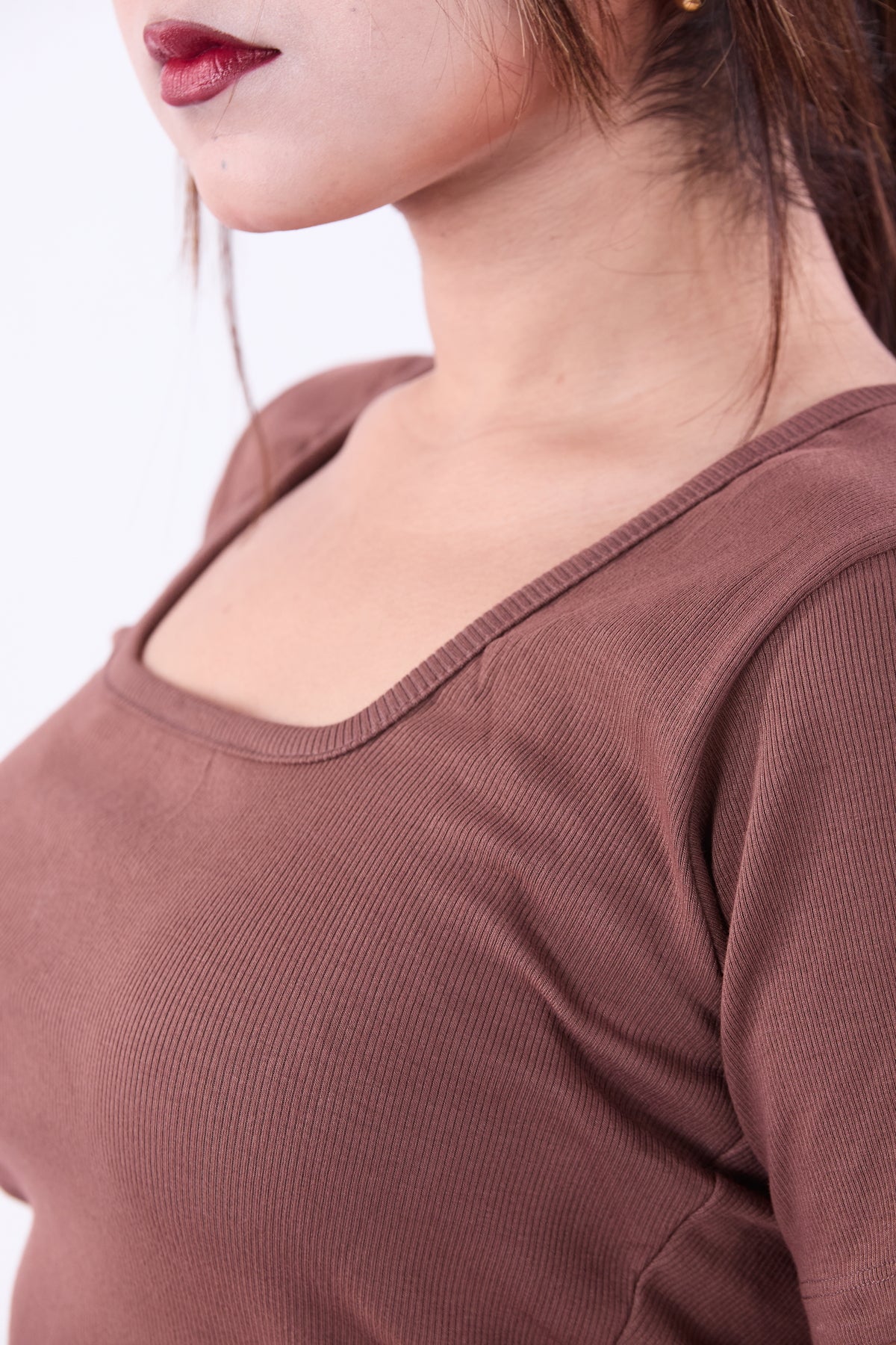 Close-up of a person wearing a brown ribbed top with a blurred background