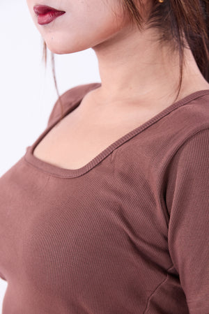 Close-up of a person wearing a brown ribbed top with a blurred background