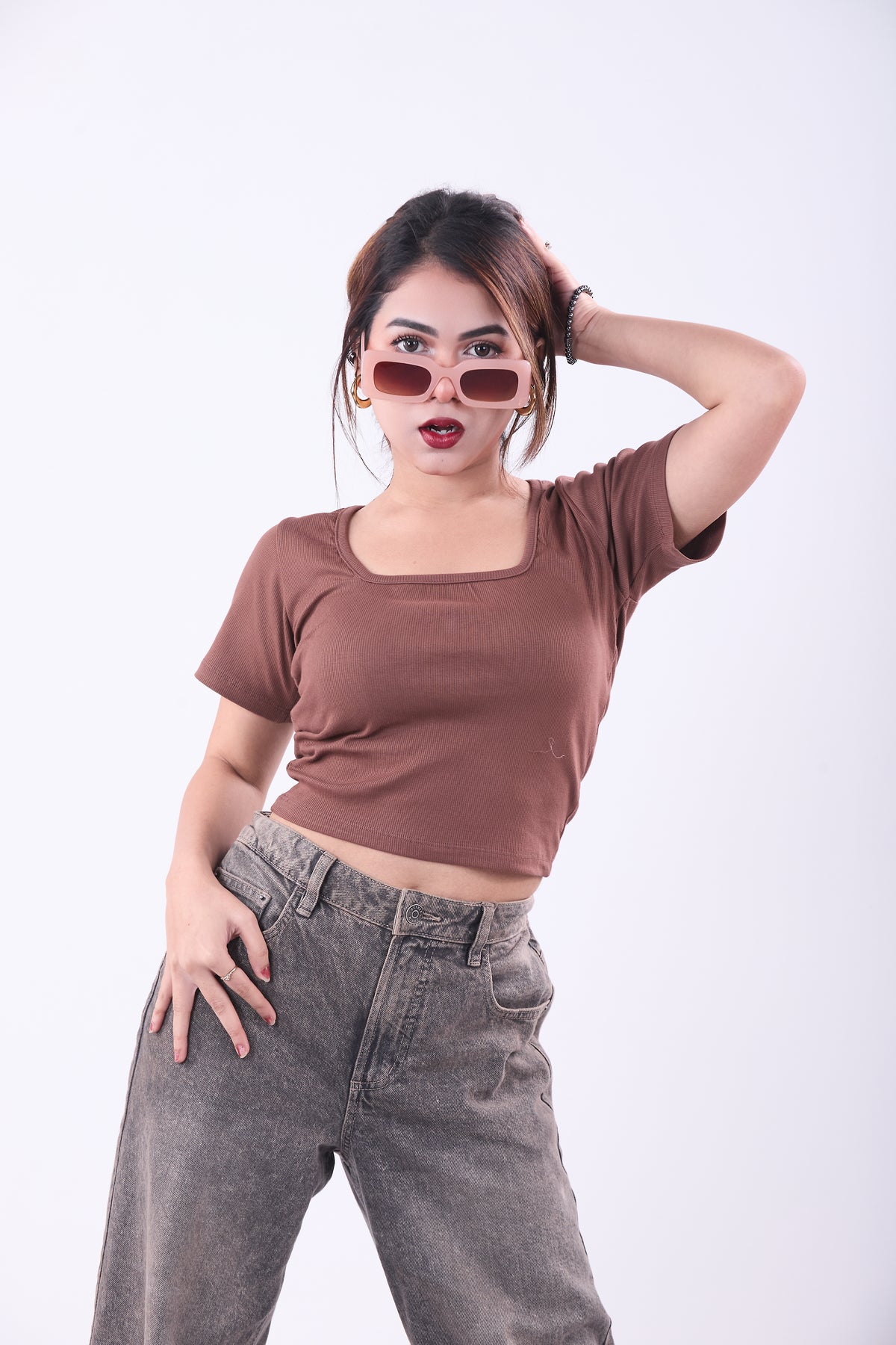Woman wearing a brown top and gray pants posing against a white background