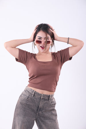 Woman wearing a brown top and gray pants with sunglasses on a white background