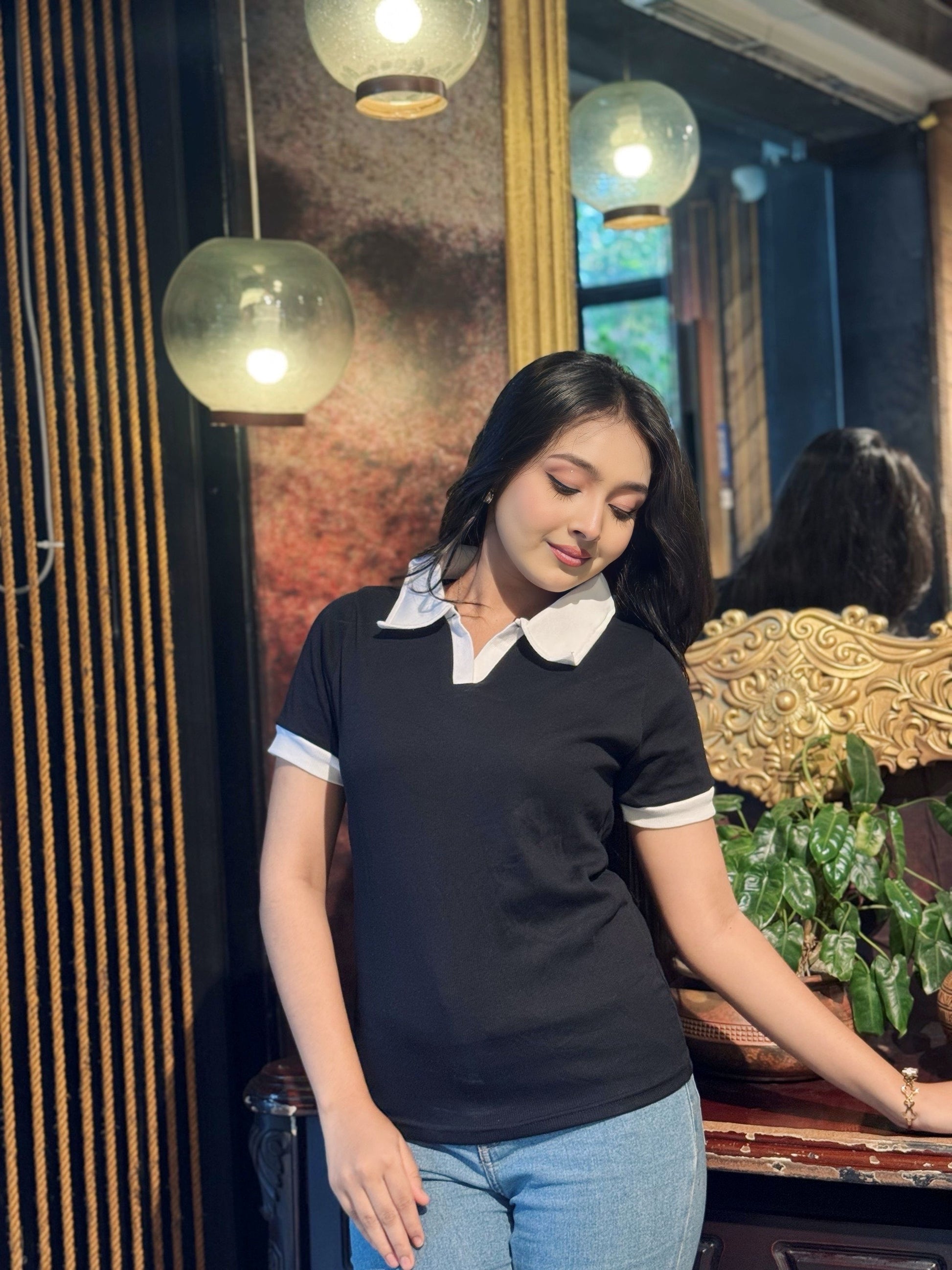 Woman wearing a black and white polo shirt in an indoor setting with decor elements.