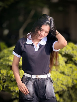 Woman adjusting her hair outdoors with a blurred green background in wearing our Black & White contrast Polo T-Shirt.