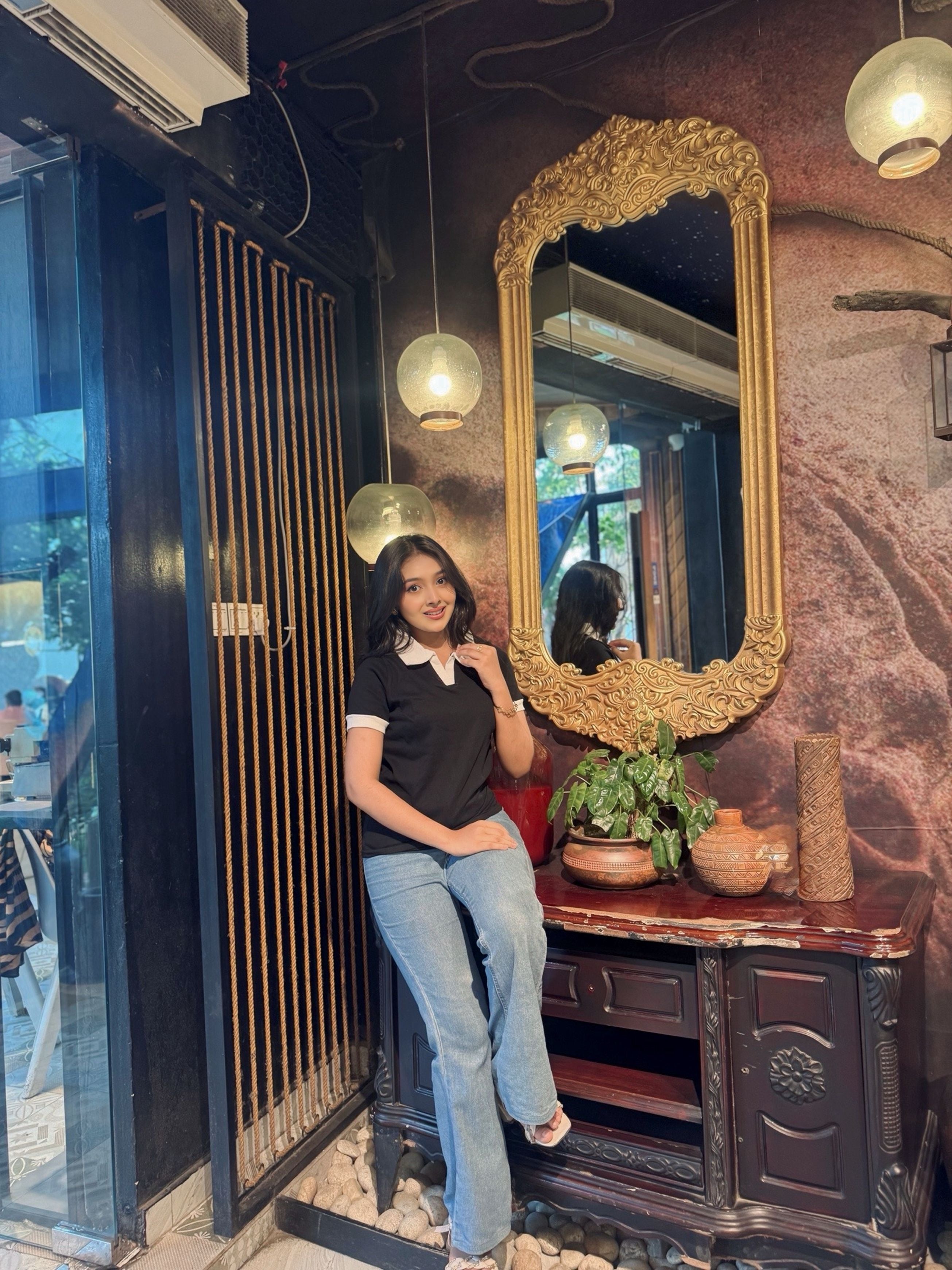 Woman sitting in a room with a large ornate mirror and decorative items in wearing our Black & White contrast Polo T-Shirt.