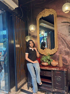 Woman sitting in a room with a large ornate mirror and decorative items in wearing our Black & White contrast Polo T-Shirt.