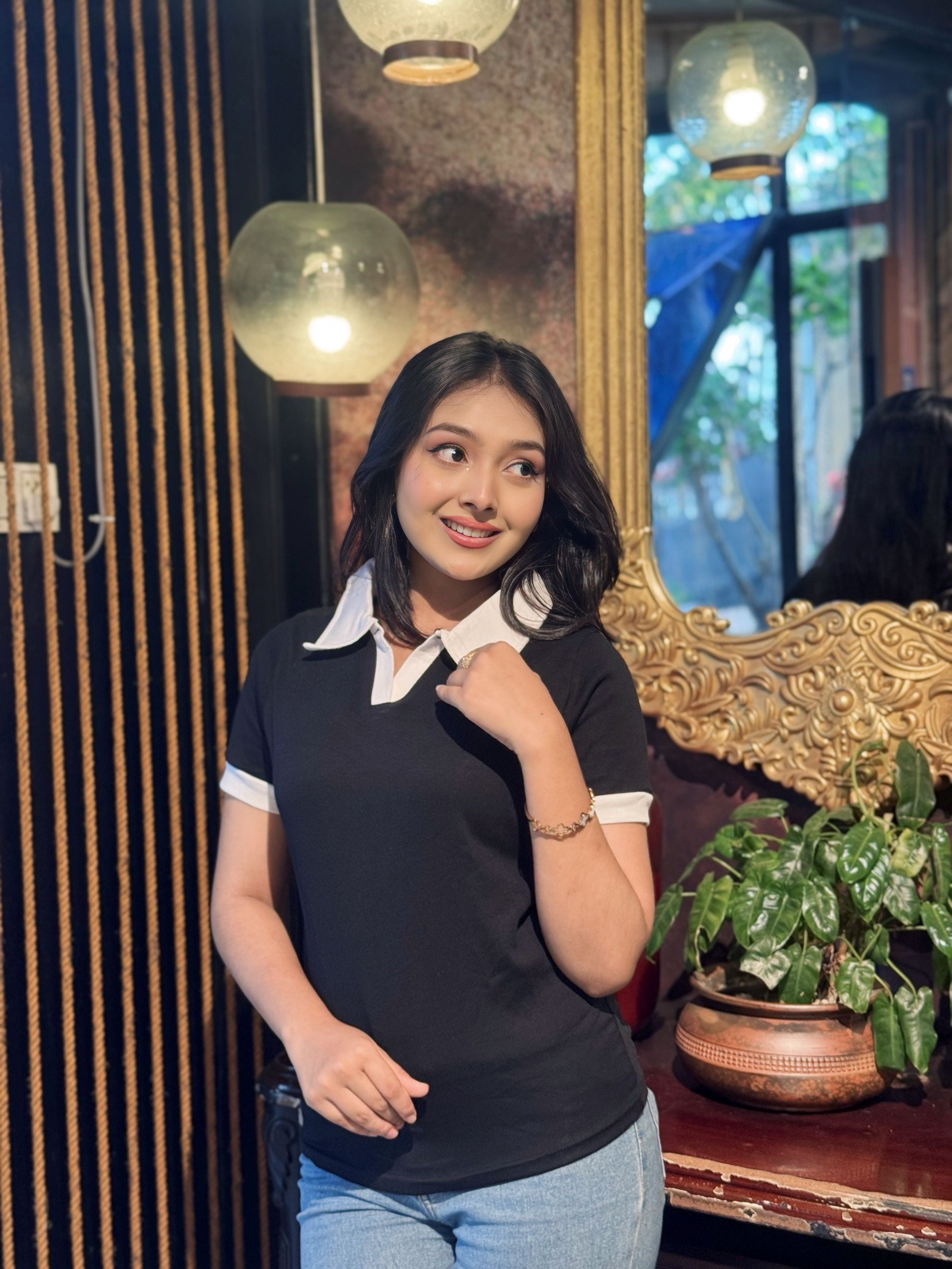 Woman posing indoors with decorative elements and plants in the background wearing our Black & White contrast Polo T-Shirt.