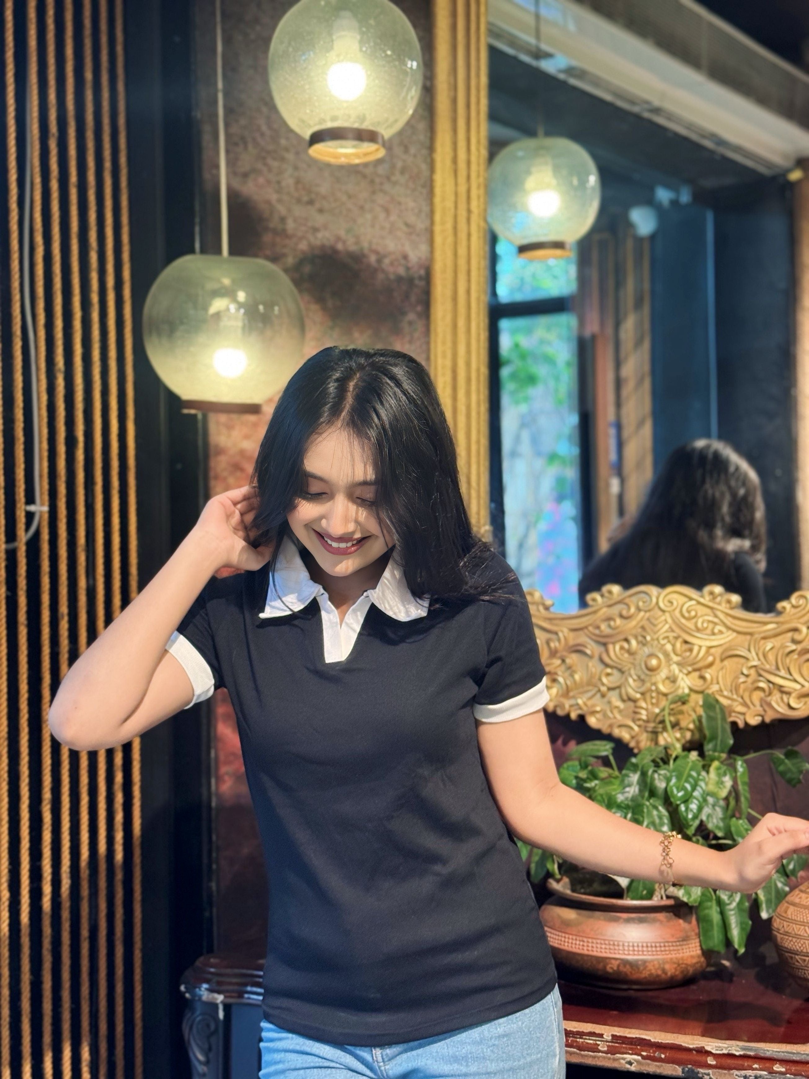 Woman adjusting her hair in a room with decorative elements and plants in wearing our Black & White contrast Polo T-Shirt