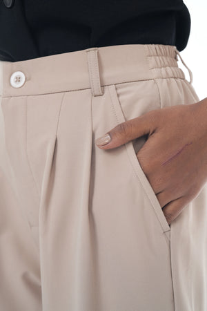Beige pleated pants with a hand in the pocket on a neutral background