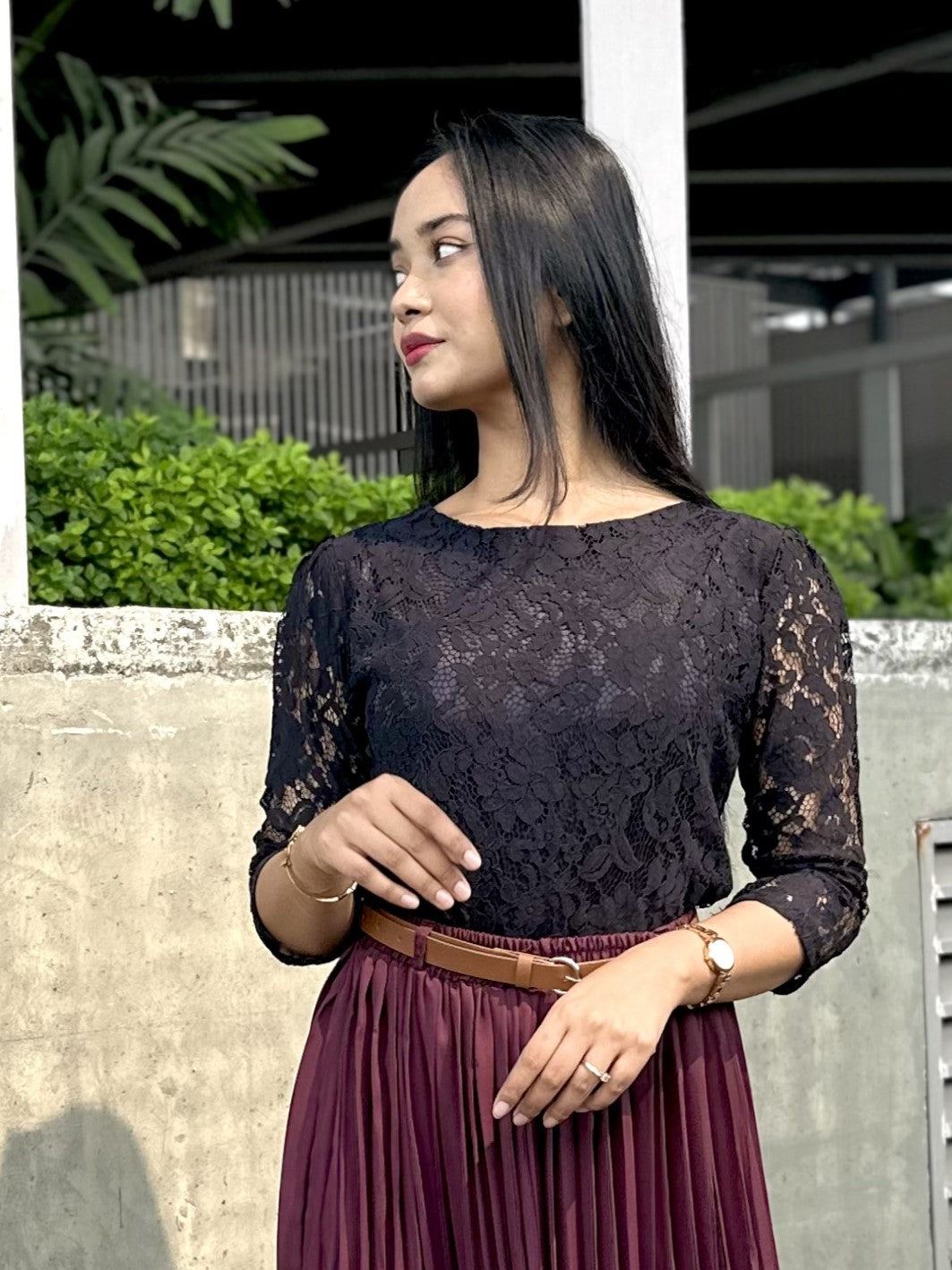 Woman wearing a black lace top and maroon skirt outdoors.