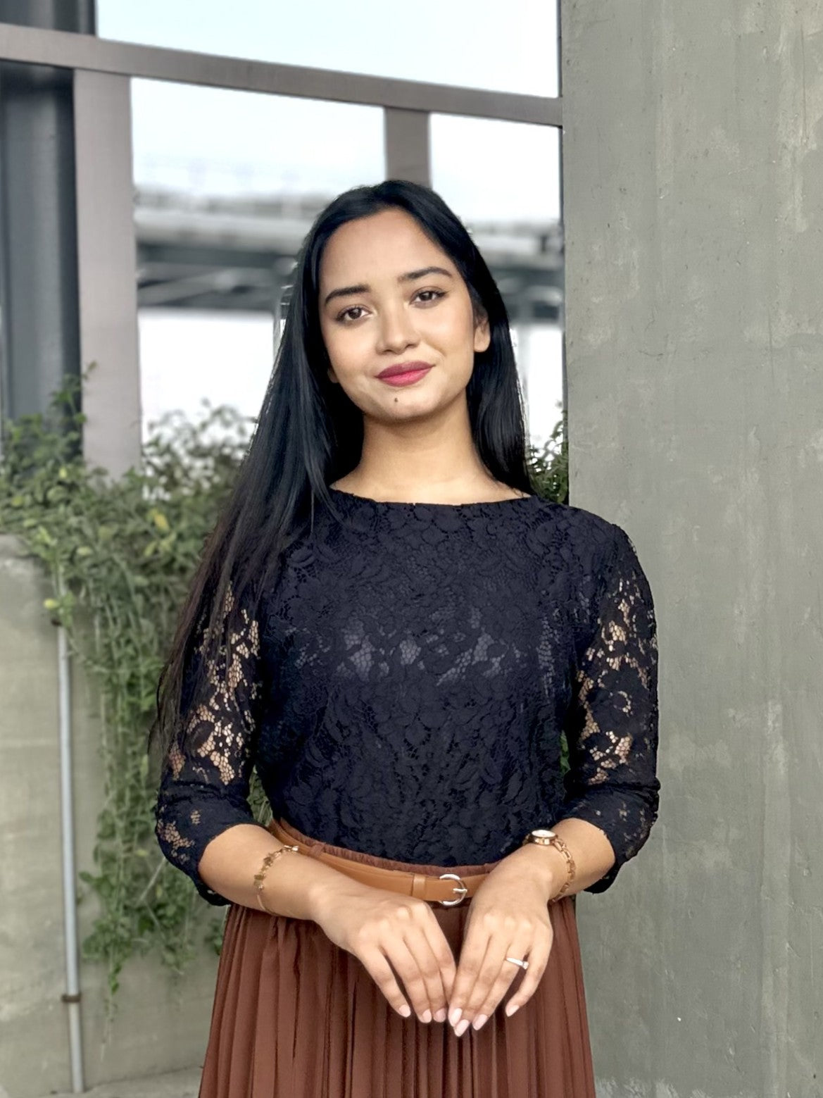 Woman wearing a black lace top and brown skirt standing outdoors.