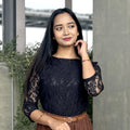 Woman wearing a black lace top and brown skirt standing against a neutral background