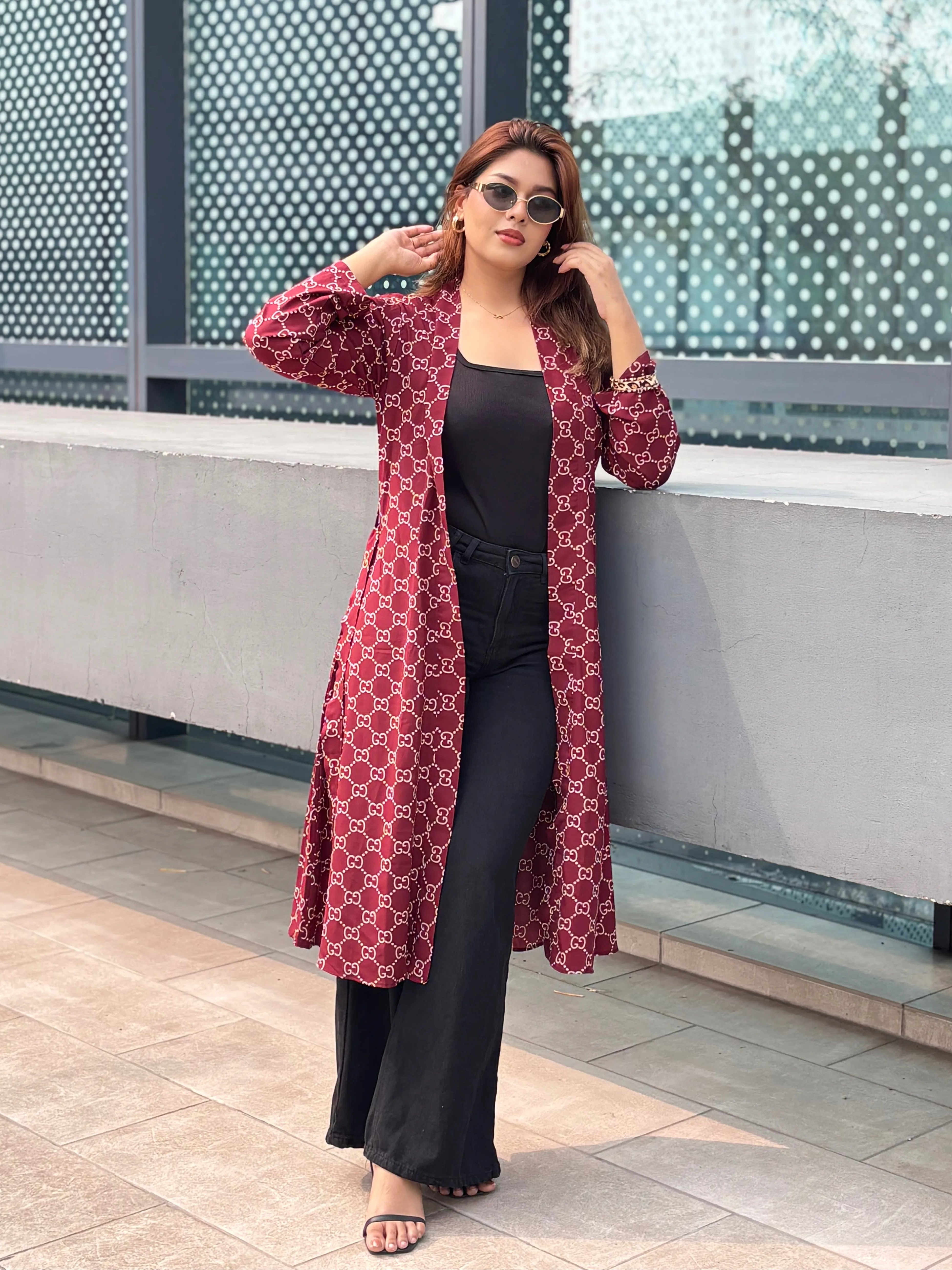 Woman wearing a red patterned Shrug and black pants standing against a modern building.