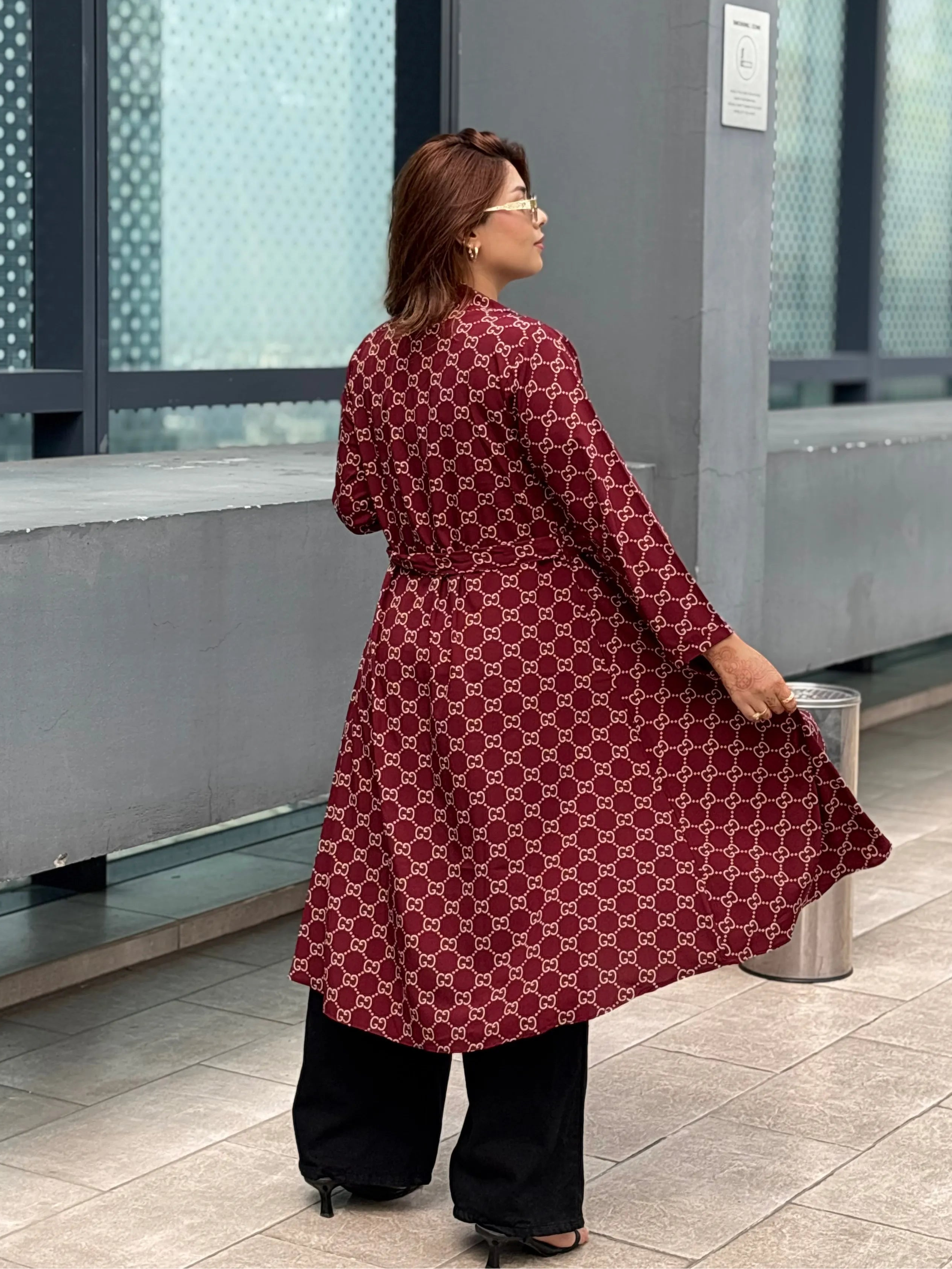 Woman in a red patterned dress standing in a modern indoor setting with large windows.